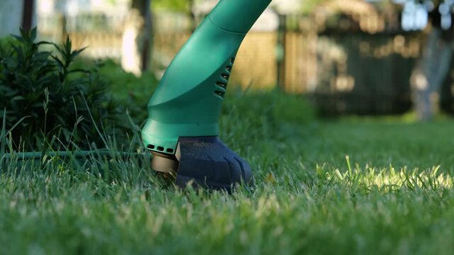 Close up of gasoline lawn-mower cutting green grass in backyard. Lawn mower mows in the garden. Slow motion. Person using lawn mower machine in yard. Gardening, outdoor concept