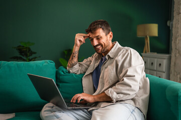 Man relaxing at home working on laptop, smiling