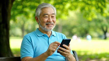 Smiling senior Asian man using smartphone in park on sunny day for communication - Powered by Adobe