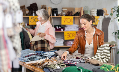 Young woman buyer choosing warm sweater in clothing store