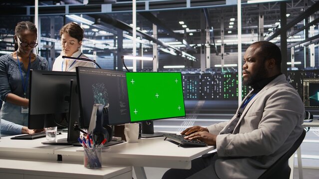 Data center admin inspecting gear using green screen mockup PC, doing maintenance tasks. African american server farm worker using chroma key computer, conducting system checks, camera A - Powered by Adobe