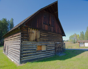 Rustic Wooden Barn With Weathered Logs On a Bright Green Field Under Clear Blue Sky. Historic Rustic Ant Flat  Kootenai National Forest in Montana. Evoking countryside charm and rural life in a serene