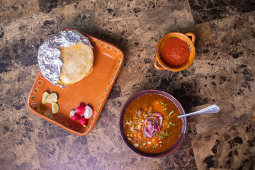 Birria stew with red onions and cilantro served next to a taco, salsa, lime, and radish