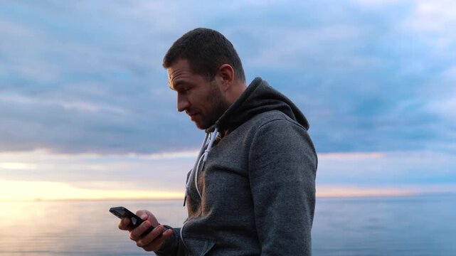 Man Speaks on the phone on a spacious coast near the sea or ocean. Sunset in the water.