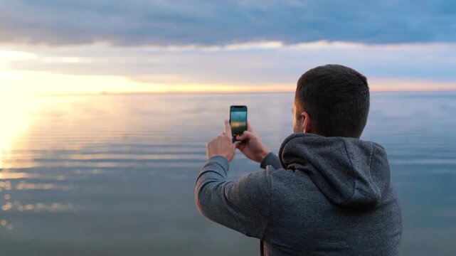 a man photographs the sunset or takes a video on the sea on the phone