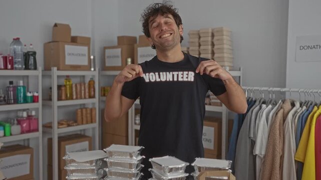 Hispanic man smiling proudly in a volunteer shirt stands in a donation room with shelves of supplies and clothing racks, embodying community support and charitable engagement.
