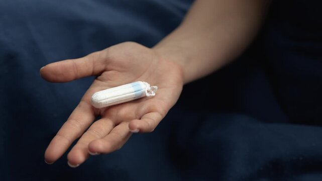 Menstrual tampon is in her hand. Hold hand on linen bedclothes. Menstruation time. Hygiene.