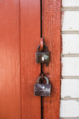 Close-up of a red-painted wooden door secured with two padlocks. Symbol of strong home protection.