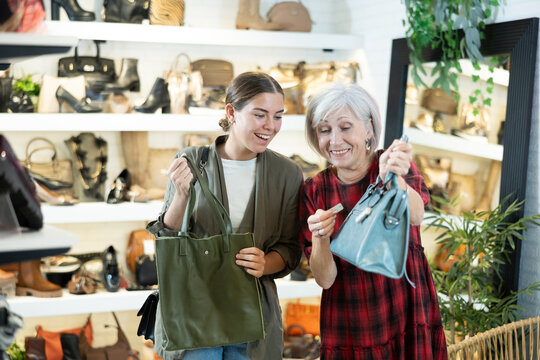 Mature woman with young daughter in store eye windowshopping product she likes and tactilely checks authenticity and naturalness of leather material from which bag is made.