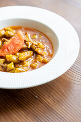 Close-Up of Traditional Okra Dish with Tomatoes on a White Plate on a Wooden Table
