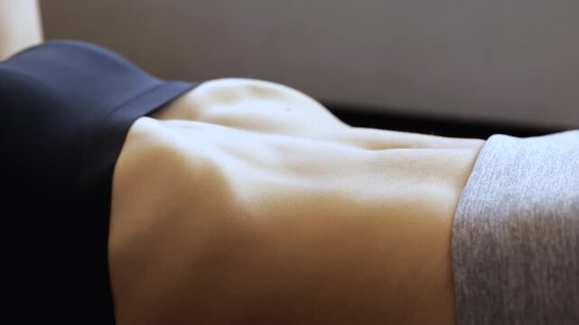 Young woman has workout at home during quarantine. Close up and side view of model training her abs muscles. Exercising hard. Strong sexy hot body.