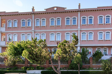 Fototapeta premium Elegant pink building with symmetrical windows and lush greenery in urban setting