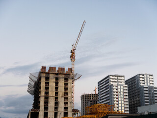 Fototapeta premium A construction site features a tall concrete building under development with a towering crane, scaffolding, and heavy equipment, creating an active urban project scene.