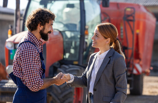 Farmer and businesswoman shaking hands in front of tractor