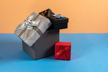 Stack of Gift Boxes in Silver, Red, and Black Ribbons on Bright Orange and Blue Backdrop