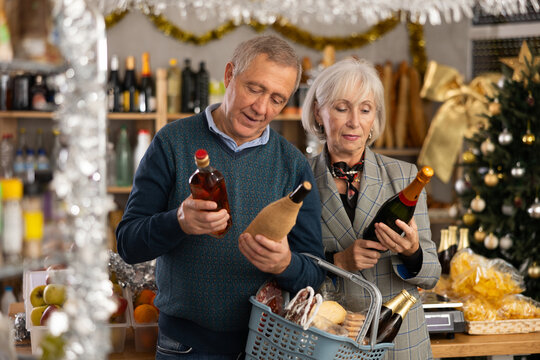 Elderly husband and wife choosing wine and whiskey for Christmas celebration at supermarket