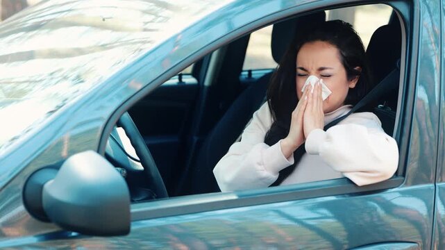 Young woman sit in car during travelling break. Sick ill girl sneezing into white tissue and sufferfrom headache. Woman in car dring short travel break. Bad health condition.