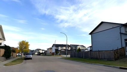 Obraz premium Tranquil Suburban Street Scene under Blue Sky with Soft Clouds