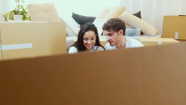 Young couple move into new apartment. Man and woman sit together on floor. Girl hold smartphone in hand and using it. Guy help her with looking for information. Relocation time.