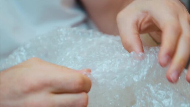 Young couple move into new apartment. Close up and cut view of man's hands playing with bubble wrap. Relaxing.