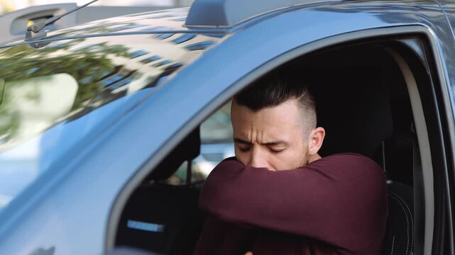 Young man inside car. Slow motion of guy caughing very bad and hard. Cover mouth with middle of hand. Suffer from coronavirus symptoms.