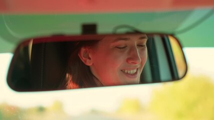 Girl driver drives her car, happy emotions. Beautiful young woman traveling by car, smiling, rejoicing, good mood. Young female driver in reflection of rearview mirror. Weekend, car, road, sports