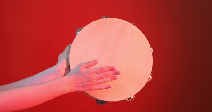 Woman playing tambourine in color light on red background, closeup