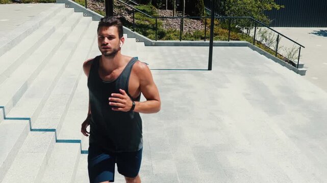 Young man exercising outside. Video of guy listening to music through white earphones and jogging alone on steps area. Exercising or doing fitness activity.