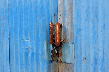 Close up of a locked blue corrugated metal door with heavy rust on the padlock, hasp, and chain....