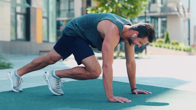 Young man exercising outside. Video process of guy doing mountain climber exercise. Running fast in horizontal position on the same place. Training near urban view.