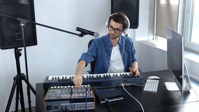 Young man in sound recording studio. Male video blogger filming hot to work with mixing console and keyboard. Musician works with sound equipment.