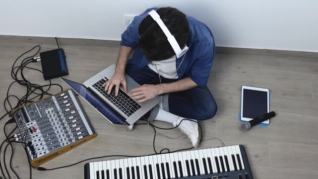 Young man in sound recording studio. Guy sit on floor and work with laptop and soung mixing console. Recording music. Microphone lying on tablet. Up view.