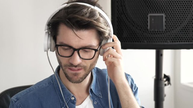Young man in sound recording studio. Slow motion of guy listening to music through headphones. Rocking alone in room and enjoy it.