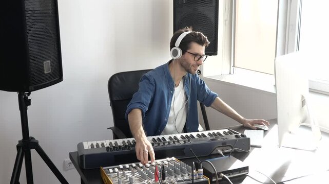 Young man in sound recording studio. Guy sit in front keyboard and using music mixing console. Listening to music through headphones and enjoy recording.