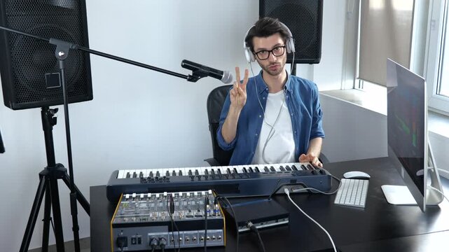 Young man in sound recording studio. Guy looks on camera and greets who's watching. Working woth professional music equipment. Adjusting sound console. Slow motion.