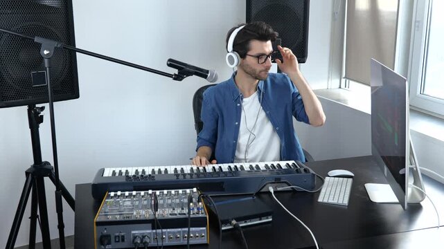 Young man in sound recording studio. Slow motion of cheerful soundman adjusting music console. Student learning how to play on keyboards.