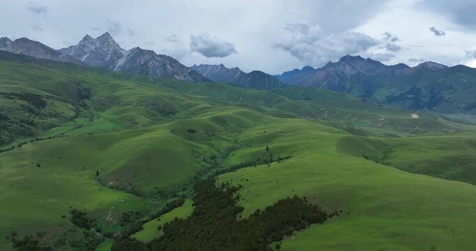 Aerial footage of beautiful high altitude snow capped mountains and forest grassland landscape in China
