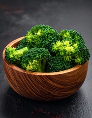 Fresh broccoli florets nestled in a wooden bowl, showcasing vibrant green hues against a dark backdrop.