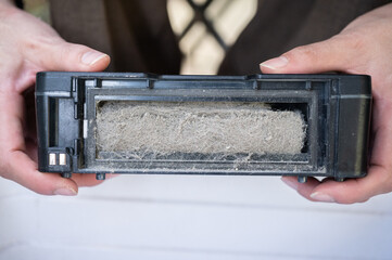 Woman holding a vacuum dust filter for cleaning it. Cleaning filter protect the overall air quality in your home as well by capturing dust, debris, and other allergens.