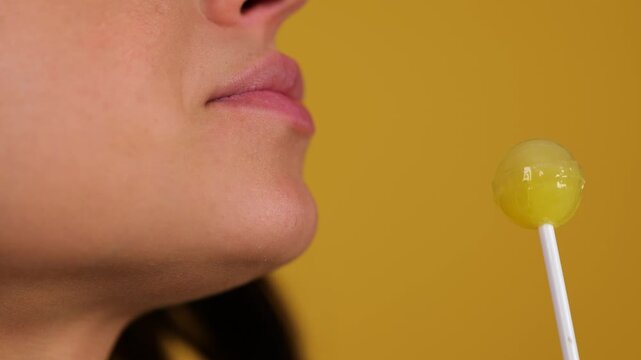 Young woman sexy eating chupa chups, close up. Woman lips sucking lollipop. Sensual concept. Copy space. Isolated yellow background. Real time