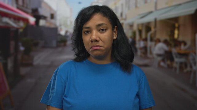 African american woman in blue shirt standing on street with visible face looking at camera; melancholy.