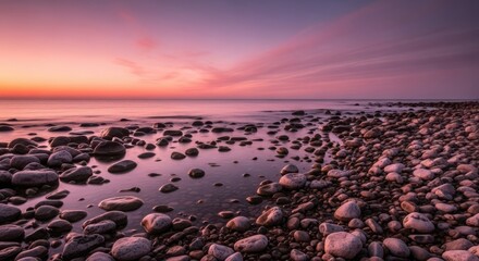 Obraz premium A serene rocky shoreline at sunset with vibrant pink and purple hues painting the sky and reflecting on the calm water, creating a tranquil and picturesque natural landscape