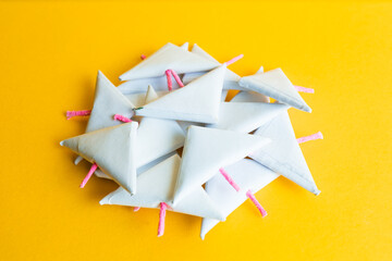 Close-up of a pile of white paper triangular-shaped firecrackers, scattered and with pink fuses, on a vibrant yellow background.