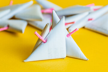 Close-up and selective focus on a pair of white paper triangular firecrackers with the pink fuses highlighted against a bright yellow background.