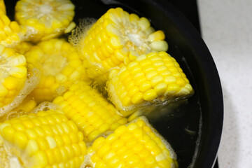 Corn pieces boiling in hot water inside a pan.