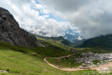 Mountain hiking trail with scenic green hills, rocky cliffs, and cloudy sky