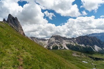 Fototapeta premium Green valley hiking trail surrounded by rocky peaks and clouds