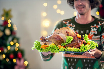 Turkey dinner Thanksgiving food. Man carry Christmas turkey food dinner Serve on table. Baked turkey chicken garnished with family Christmas tree and burning candles . Roasted turkey table setting