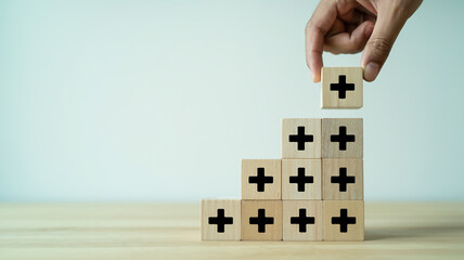 Hand placing wooden block with plus sign on top of pyramid structure