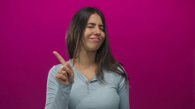 Young hispanic woman pointing her index finger with a dismissive gesture in an isolated pink studio setting; denial.